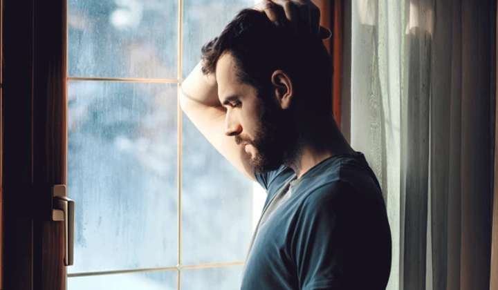 A man standing by a window thinking about the consequences of IgAN A man standing by a window thinking about the consequences of IgAN